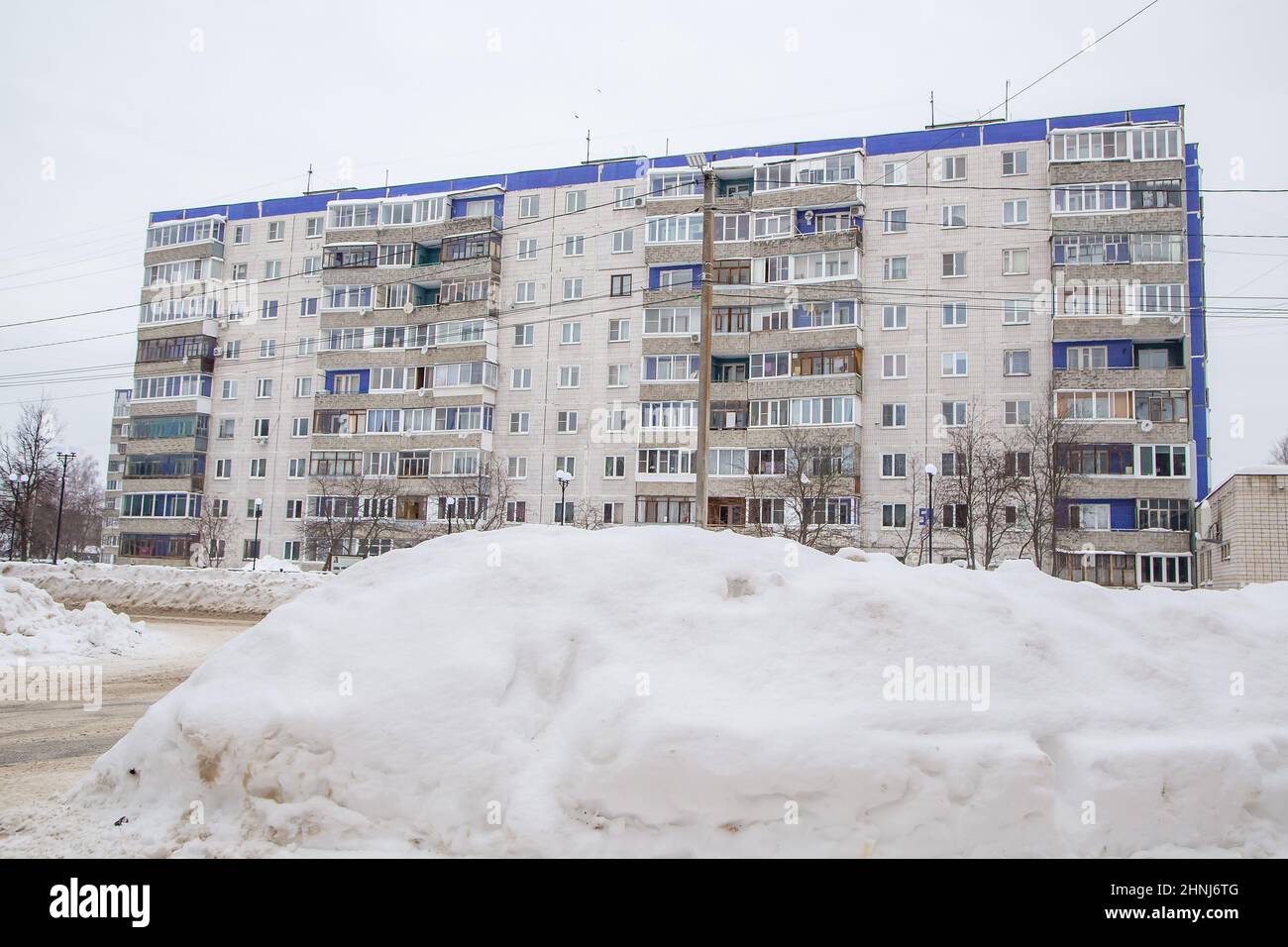 Una grande nevicata sulla strada contro lo sfondo delle case della città. Sulla strada si trova neve sporca in cumuli alti. Paesaggio urbano invernale. Nuvoloso giorno d'inverno, luce tenue. Foto Stock
