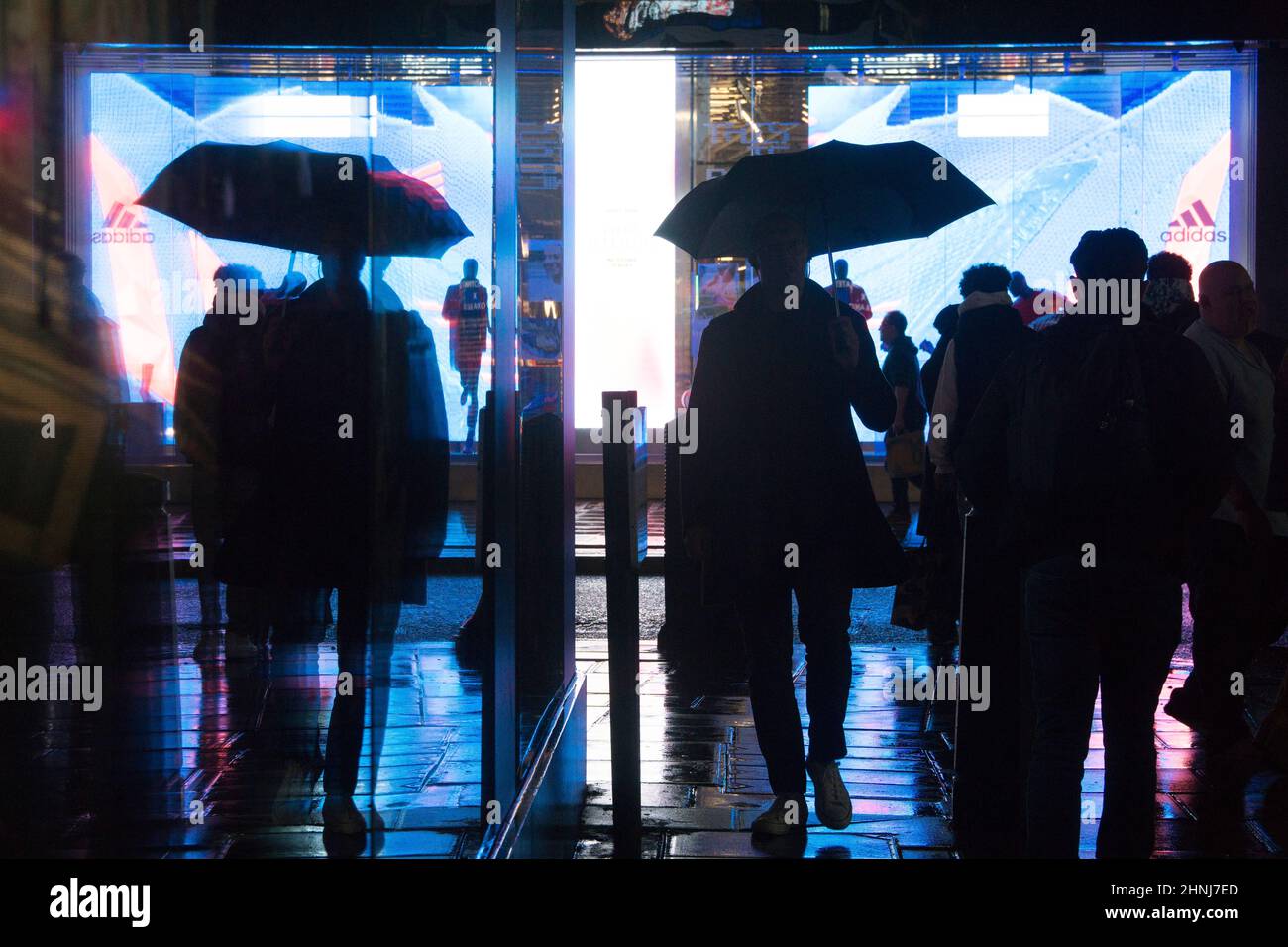 Londra, UK, 16 febbraio 2022: Su Oxford Street, un enorme schermo a LED si riflette dai marciapiedi e lungo una strada laterale in una serata piovosa. Gli acquirenti e i pendolari con ombrelloni o e-scooters sono in perfetto contrasto con le luci brillanti. L'economia si sta ribellando dopo la pandemia e la fiducia dei consumatori sembra tornare nonostante le preoccupazioni per il costo della vita di crisi. Anna Watson/Alamy Live News Foto Stock