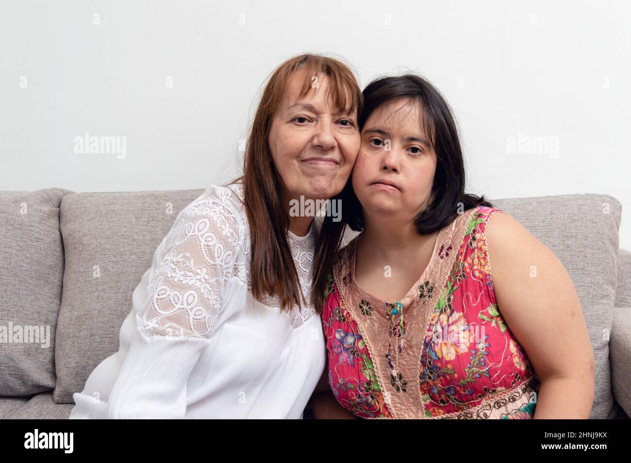 madre e figlia del latino argentino caucasico seduti sul divano nel soggiorno con le guance insieme in posa guardando la macchina fotografica, più vivo Foto Stock