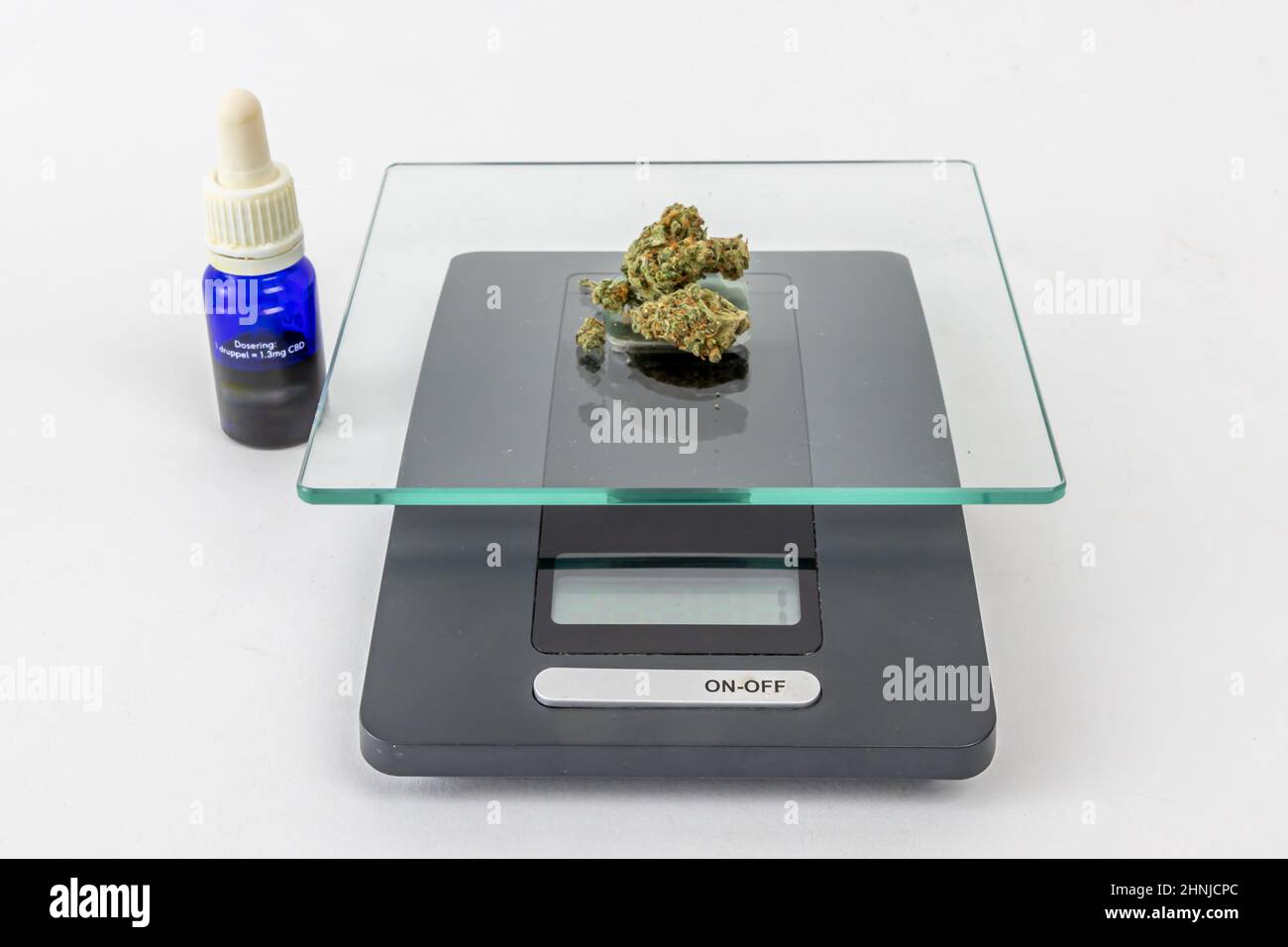 Un grammo di germogli di marijuana medica essiccati su una scala, 10ml bottiglie di vetro blu di olio CBD su uno sfondo bianco studio. Estratto di cannabis. Alternativa lei Foto Stock