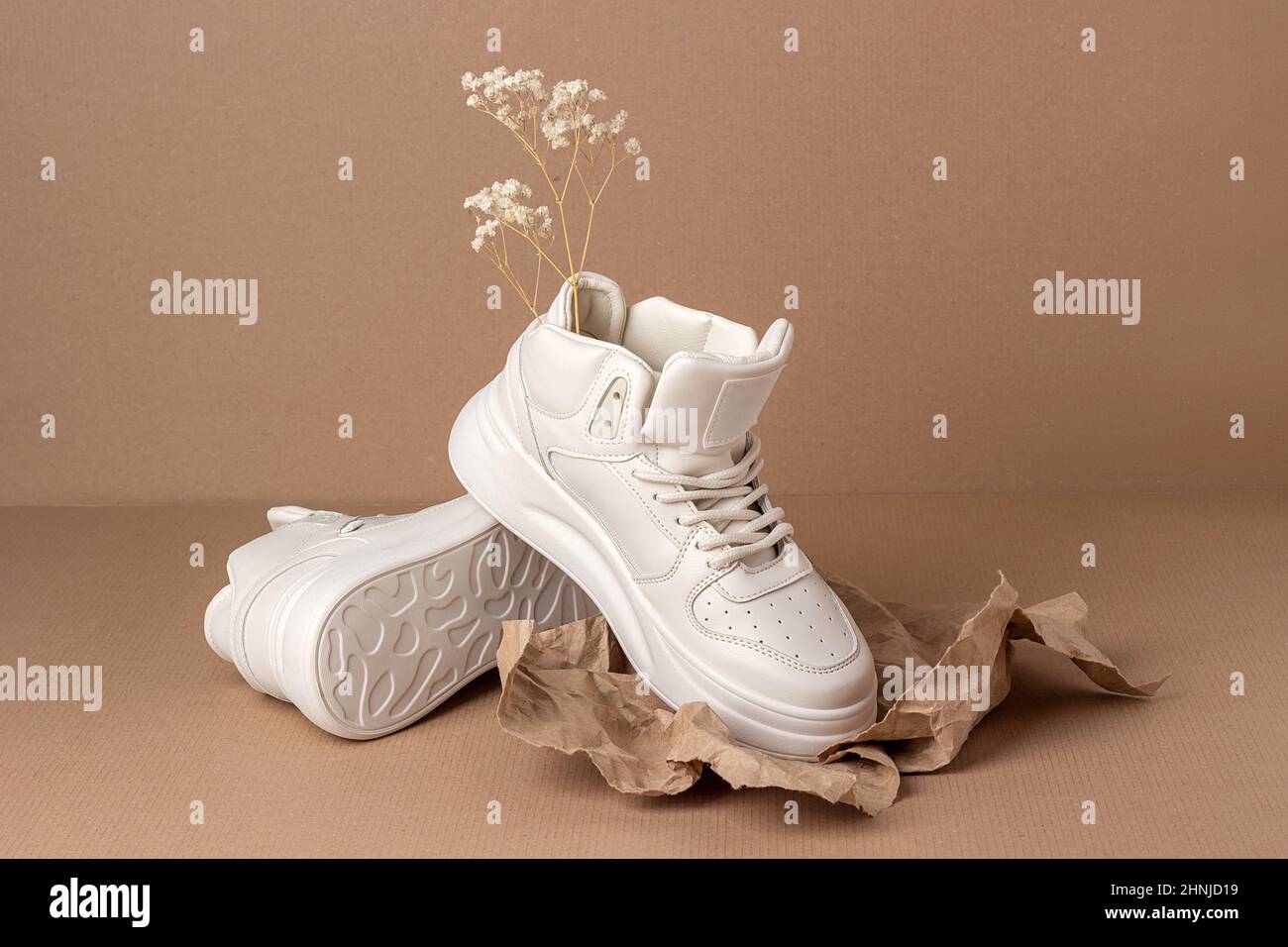 Scarpe ecologiche in pelle. Un paio di sneaker beige con fiori secchi su sfondo marrone. Stile di vita sportivo informale. Foto Stock