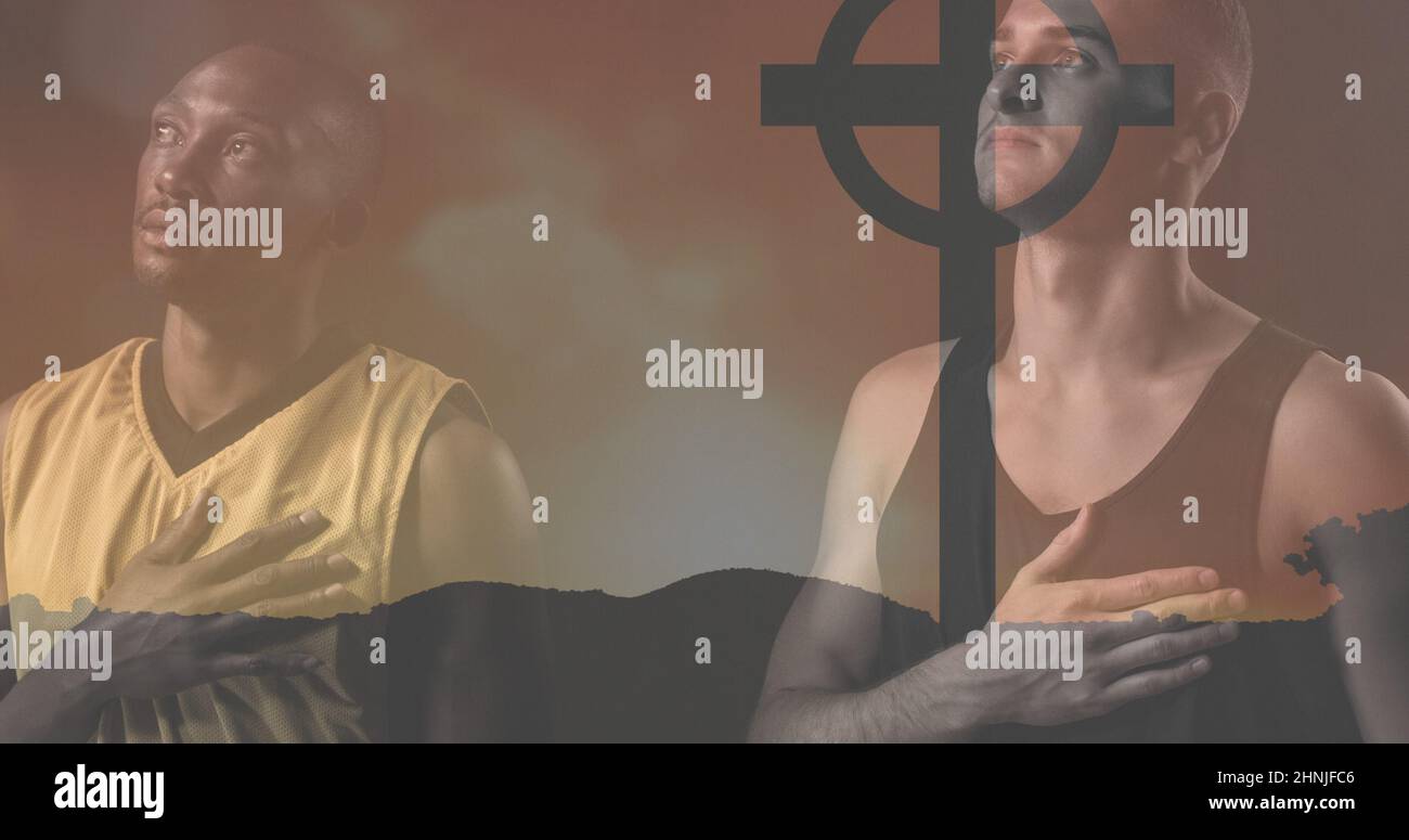 Uomini caucasici e afroamericani per adulti di media età con mano sul petto che pregano con la croce del cimitero sulla terra Foto Stock