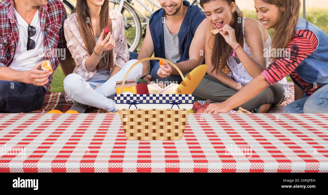 Felice caucasico giovani amici mangiare cibo mentre si siede su coperta da picnic con cestino nel parco Foto Stock