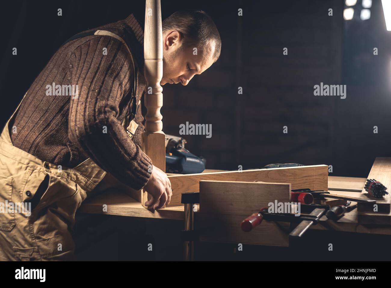 Un uomo produce prodotti in legno con l'aiuto di attrezzi speciali. Ritratto di un giovane falegname al lavoro. Occupazione nel settore della lavorazione del legno Foto Stock