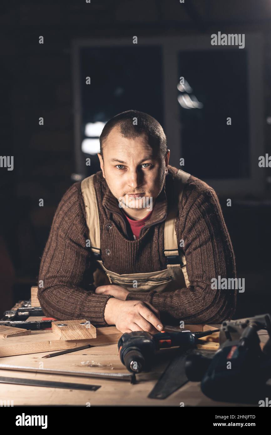Un uomo produce prodotti in legno con l'aiuto di attrezzi speciali. Ritratto di un giovane falegname al lavoro. Occupazione nel settore della lavorazione del legno Foto Stock