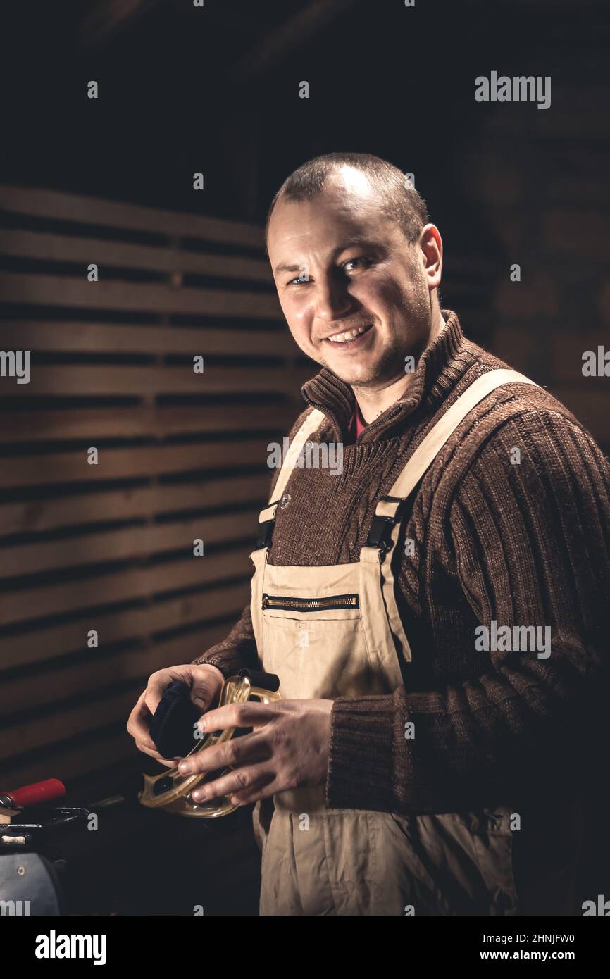 Un uomo produce prodotti in legno con l'aiuto di attrezzi speciali. Ritratto di un giovane falegname al lavoro. Occupazione nel settore della lavorazione del legno Foto Stock
