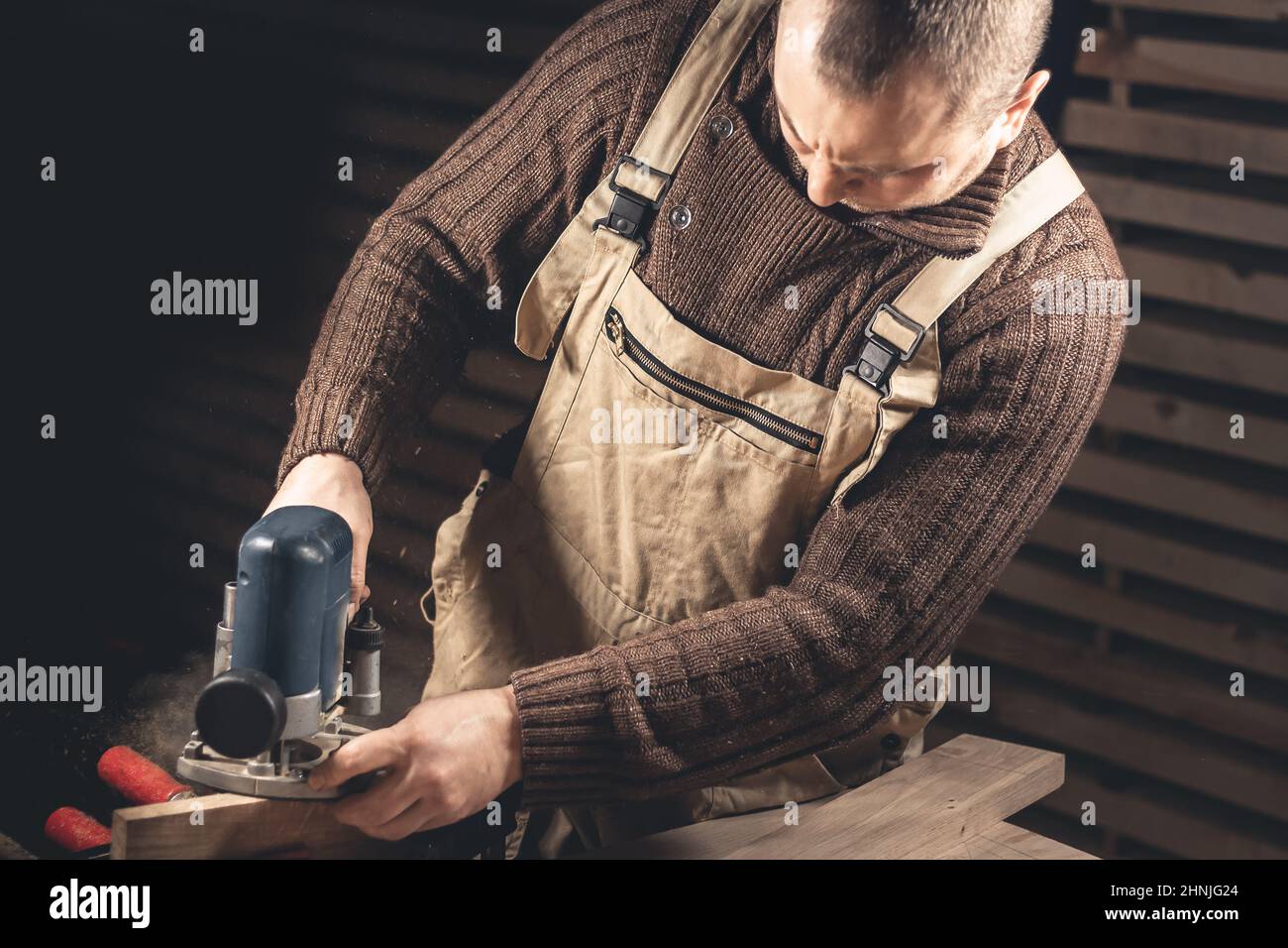 Un uomo produce prodotti in legno con l'aiuto di attrezzi speciali. Ritratto di un giovane falegname al lavoro. Occupazione nel settore della lavorazione del legno Foto Stock