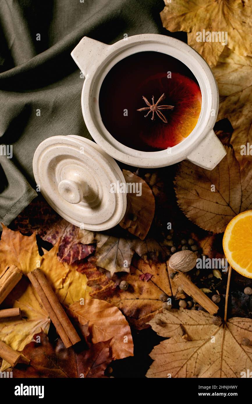 VIN brulé caldo in vaso di ceramica con spezie, foglie d'arancia e d'autunno su tovaglia di lino scuro. Disposizione piatta. Bevande alcoliche calde e accoglienti. Disposizione piatta Foto Stock