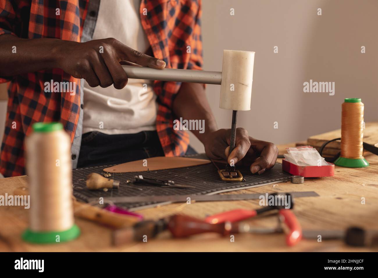 Sezione intermedia del giovane artigiano afro-americano che fa fibbia per cintura in laboratorio di cuoio Foto Stock