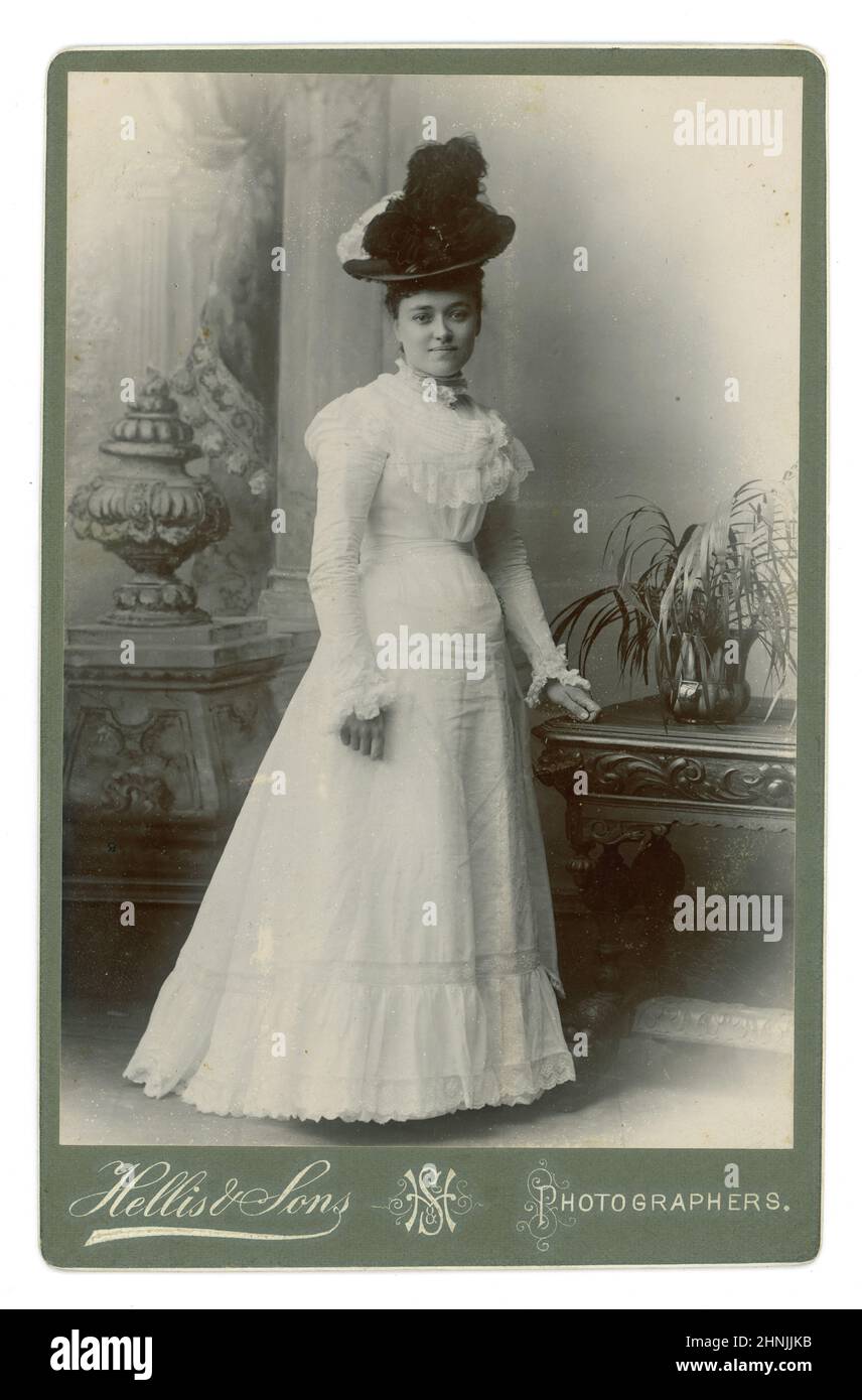 Originale tessera Edoardiana di una giovane donna edoardiana elegante, attraente e alla moda, che indossa un cappello con una piuma di struzzo e un abito estivo bianco. Signora vittoriana. Signora edoardiana. Dallo studio di Hellis & Sons, Londra, Inghilterra, Regno Unito circa 1901. Foto Stock