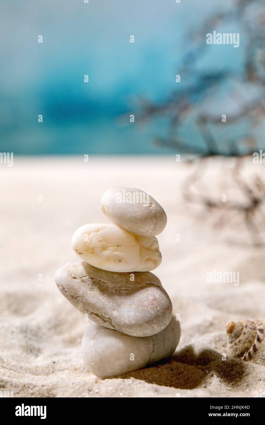 Stack di diverse pietre bianche lisce in composizione equilibrante sulla spiaggia di sabbia di mare estate con onde e conchiglie. Concetto di equilibrio di vacanza. Foto Stock