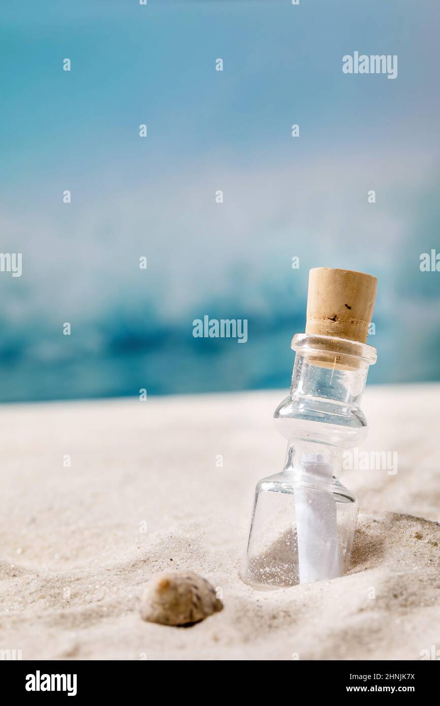 Bottiglia di vetro con carta per messaggi all'interno sulla spiaggia di sabbia marina estiva con conchiglie e onde sullo sfondo. Aiuto SOS concetto di messaggio destino. Foto Stock