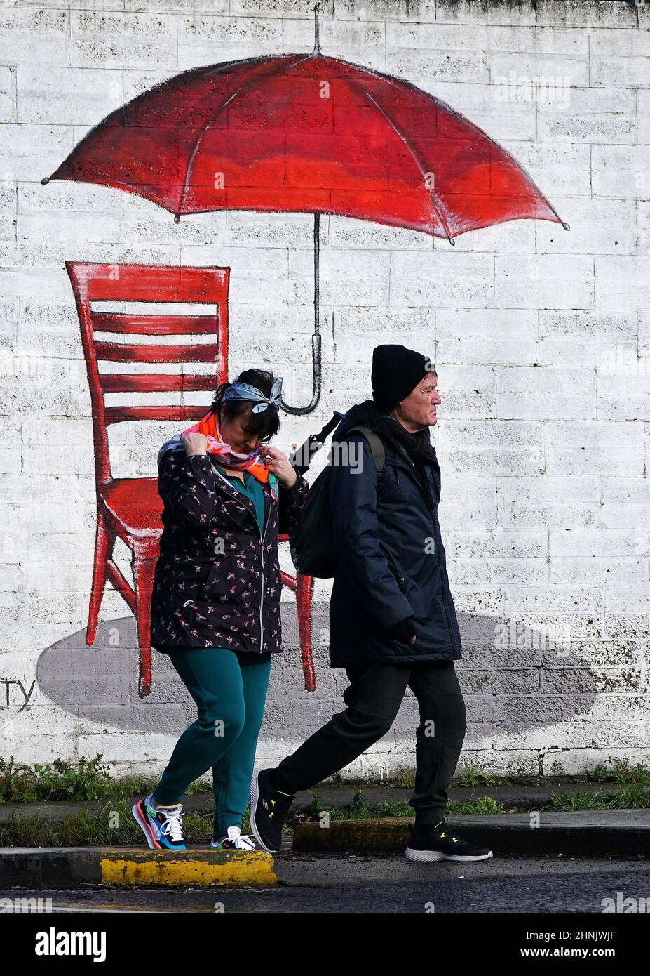 La gente cammina davanti ad un murale di un ombrello rosso a Dublino mentre le scuole e le università in sette contee nella Repubblica d'Irlanda devono essere chiuse il venerdì dopo che il Met Eireann ha emesso l'alto livello di allerta, un avvertimento di vento rosso, per Cork e Kerry. Data immagine: Giovedì 17 febbraio 2022. Foto Stock