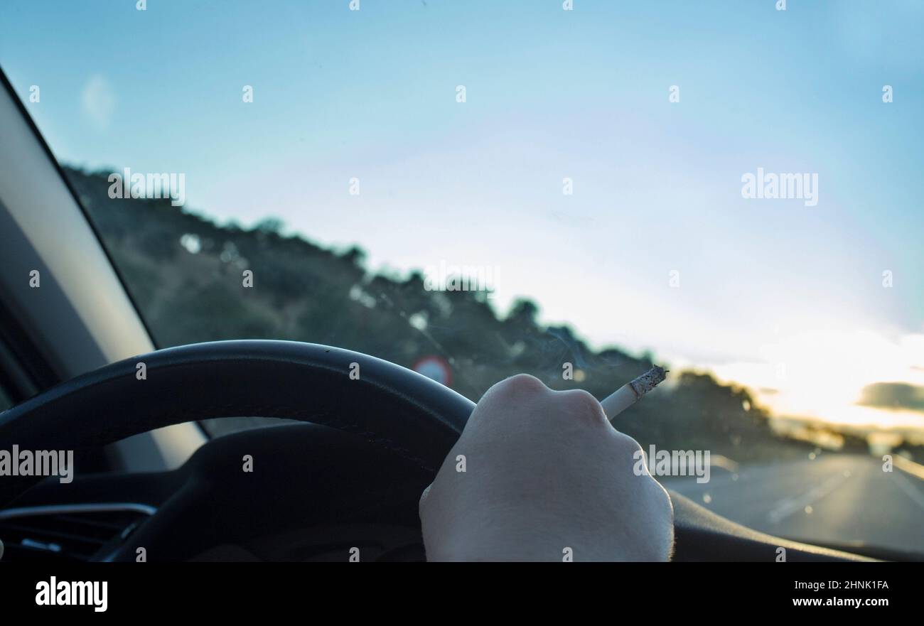 Donna che fuma durante la guida. Concetto di causa di incidenti stradali distratti. Vista interna dell'auto Foto Stock