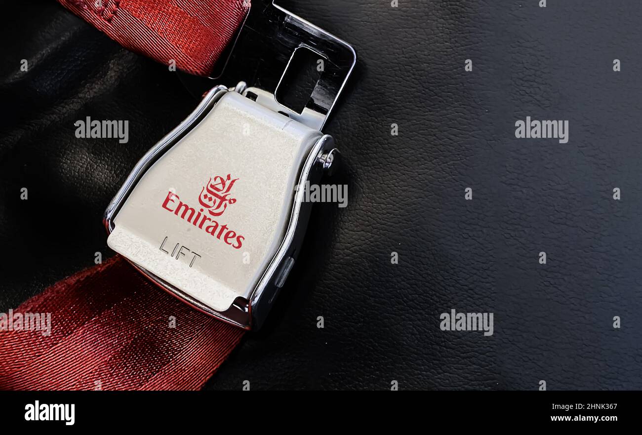Cintura di sicurezza rossa di un sedile vuoto all'interno di un aeroplano con il logo Emirates stampato sul metallo. Foto Stock
