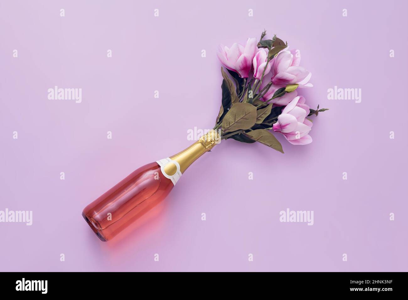 Bottiglia di champagne rosato con fiori disposti diagonalmente su sfondo viola con spazio copia Foto Stock