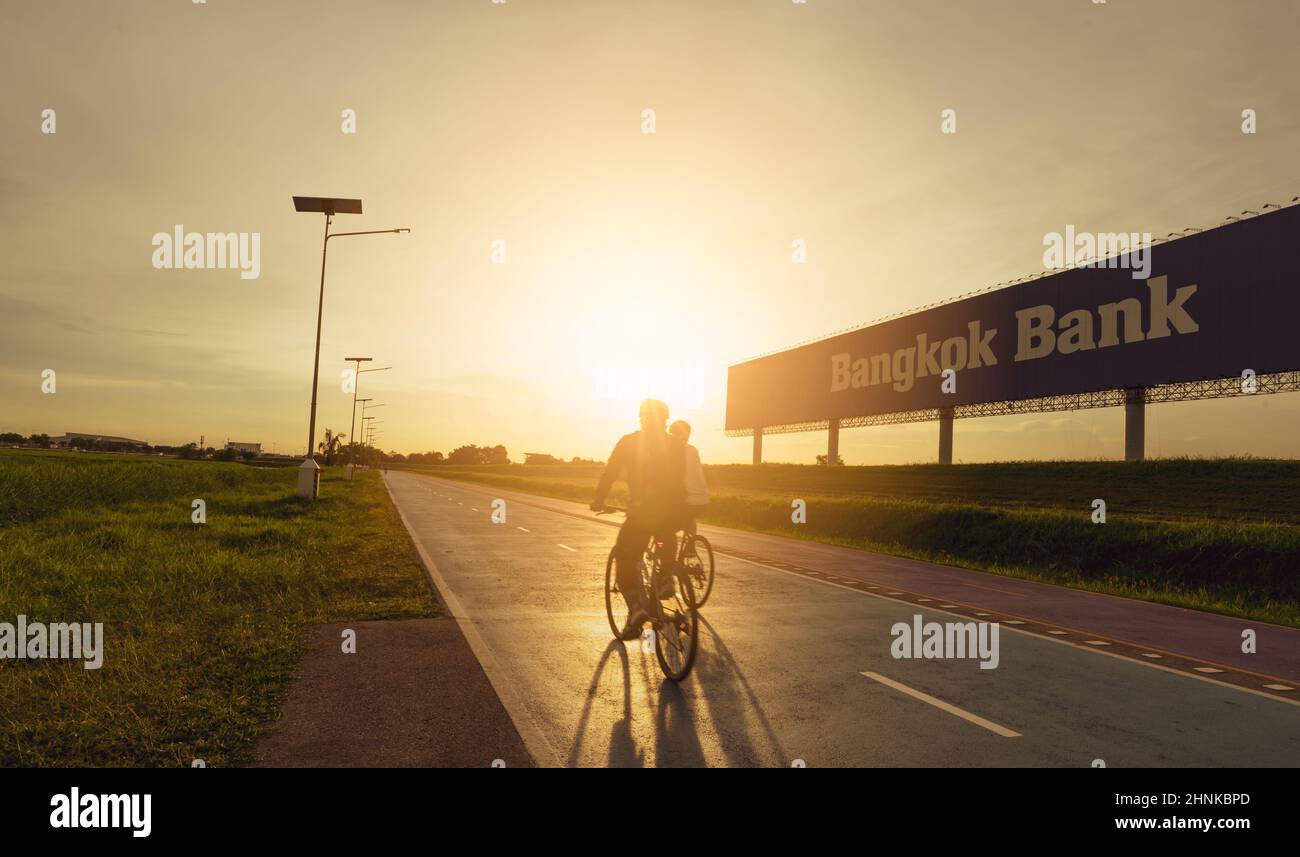 SAMUT PRAKAN, THAILANDIA-18 GIUGNO 2021 : Sport uomo giro biciclette sulla strada in serata vicino Bangkok Bank pubblicità cartellone con cielo al tramonto. Esercizio estivo all'aperto per una vita sana e felice. Foto Stock
