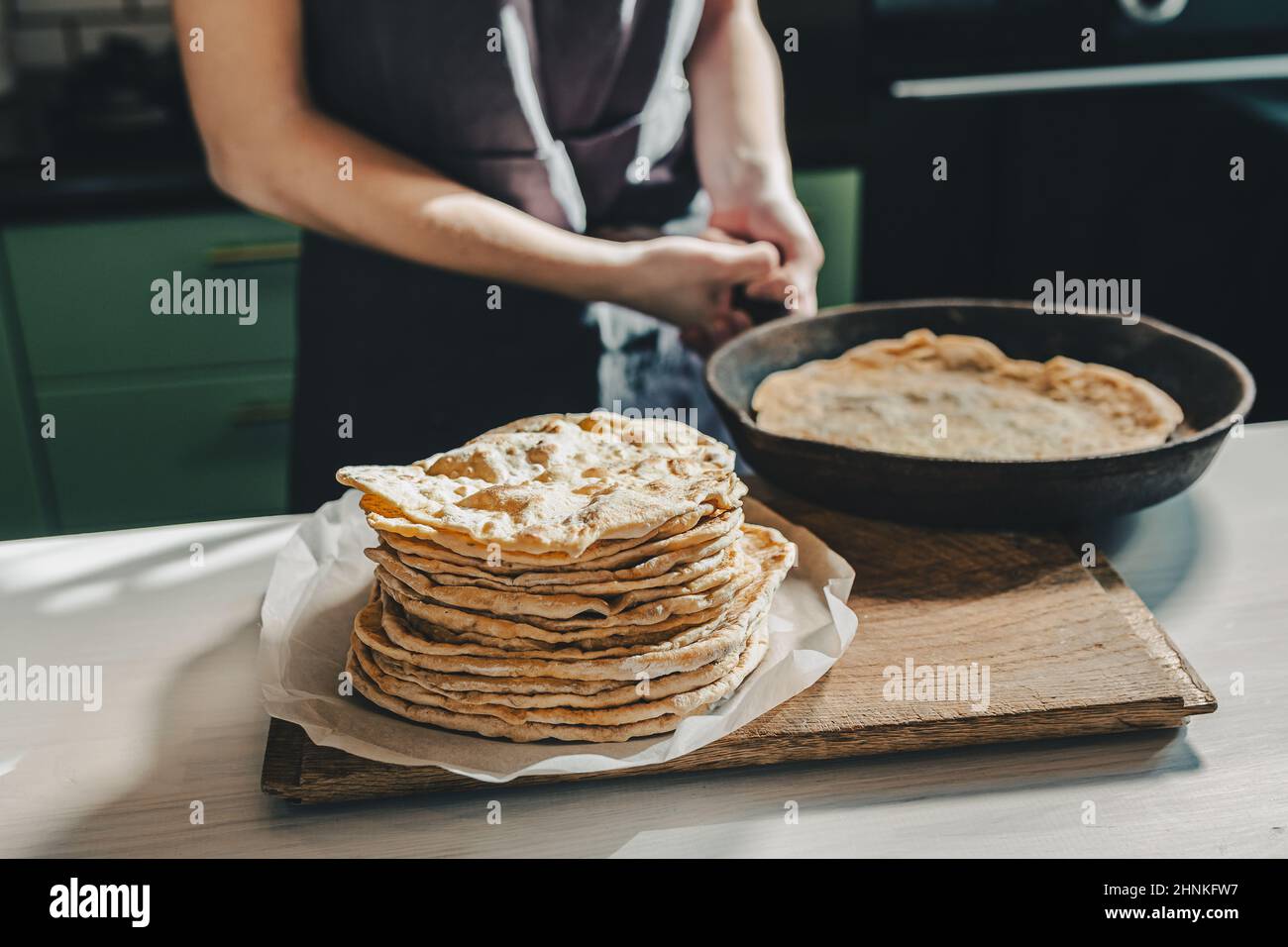 le mani di baker stanno rimuovendo il pane pita da una padella in ghisa. Mini panificio privato che produce pane artigianale e pita pane. panettiere in grembiule in cucina Foto Stock