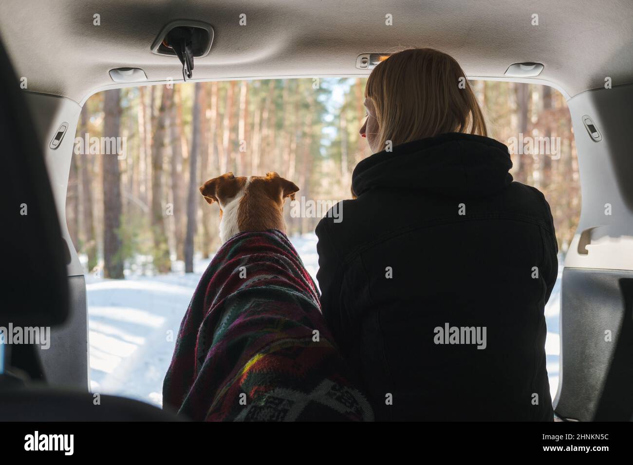 Campeggio invernale con animali domestici scena: La donna si siede accanto ad un cane in tronco SUV. Godetevi la primavera e il sole nella foresta, esplorando la natura con gli animali domestici Foto Stock