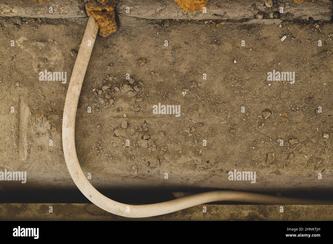 Cavo bianco che sporge dalla parete. Processo di cablaggio. Sfondo in pietra grigia Foto Stock