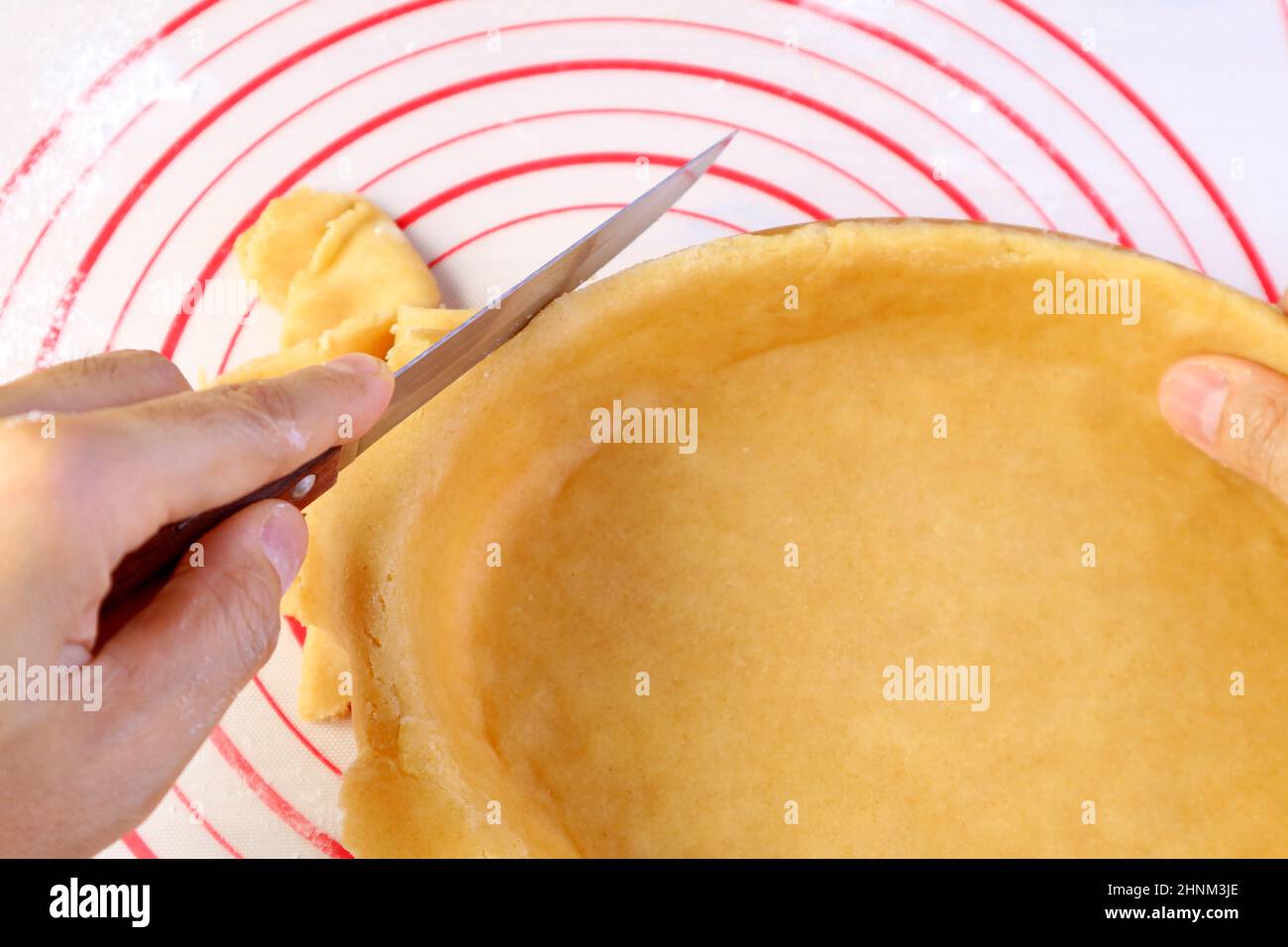 Tagliare a mano l'impasto in eccesso dal recipiente da forno prima di cuocere la crosta Foto Stock