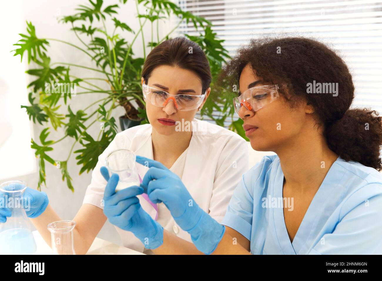 COVID-19 Test Lab. Due donne scienziati di laboratorio medico colleghi che indossano occhiali che lavorano con provette, studenti universitari multietnici worki Foto Stock