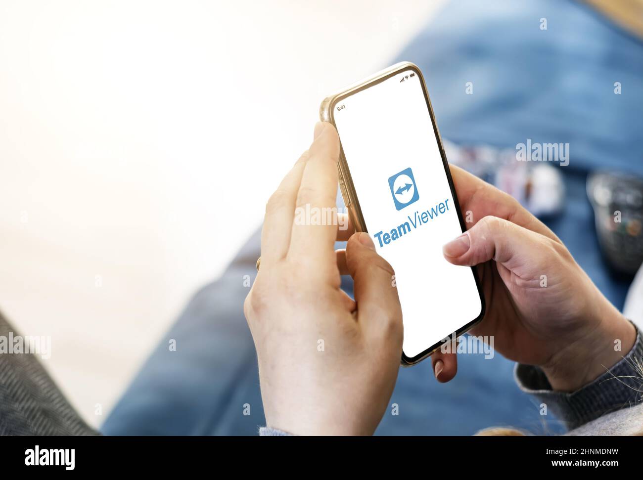 Donna che utilizza l'applicazione mobile TeamViewer per controllare in remoto il proprio computer desktop. Foto Stock