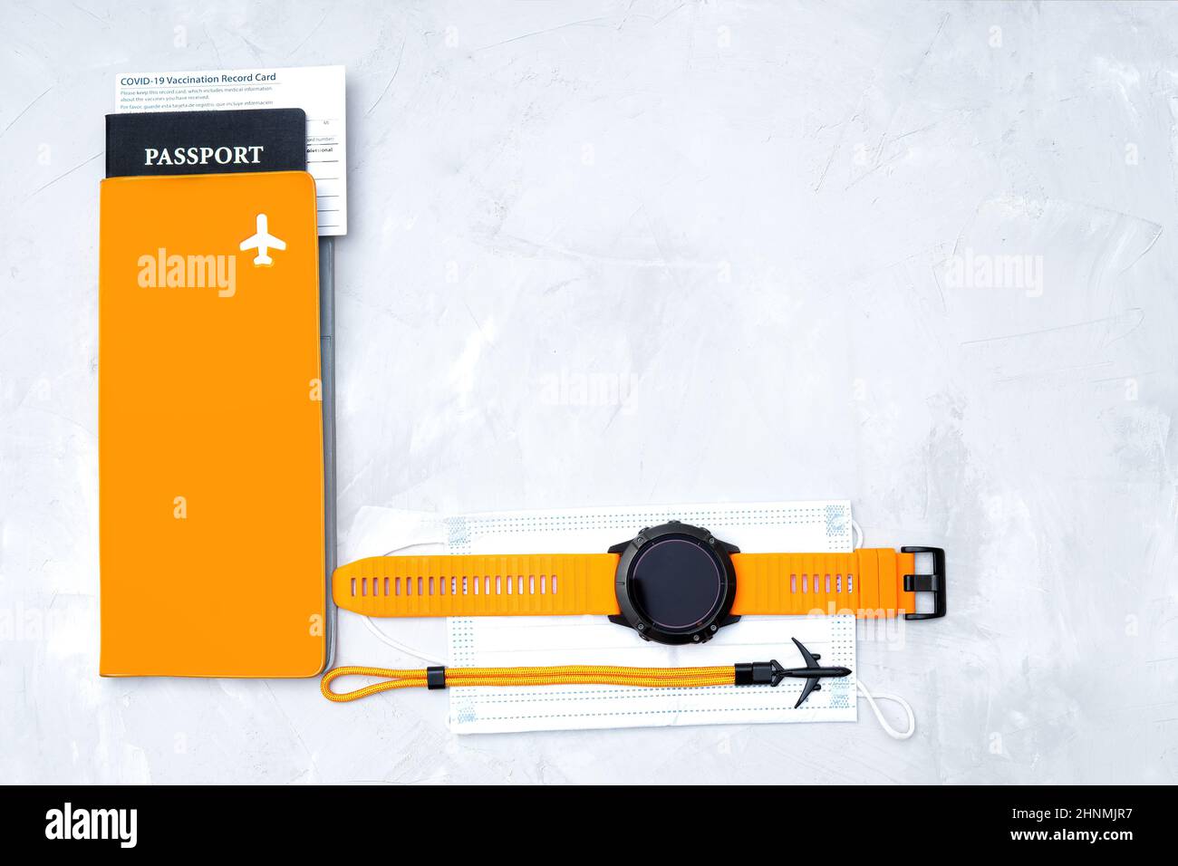 Covid-19 concetto di viaggio pandemico: Passaporto, scheda di registrazione vaccinazione, maschera facciale, organizer di documenti, smartwatch sportivo e un braccialetto aereo su un con Foto Stock