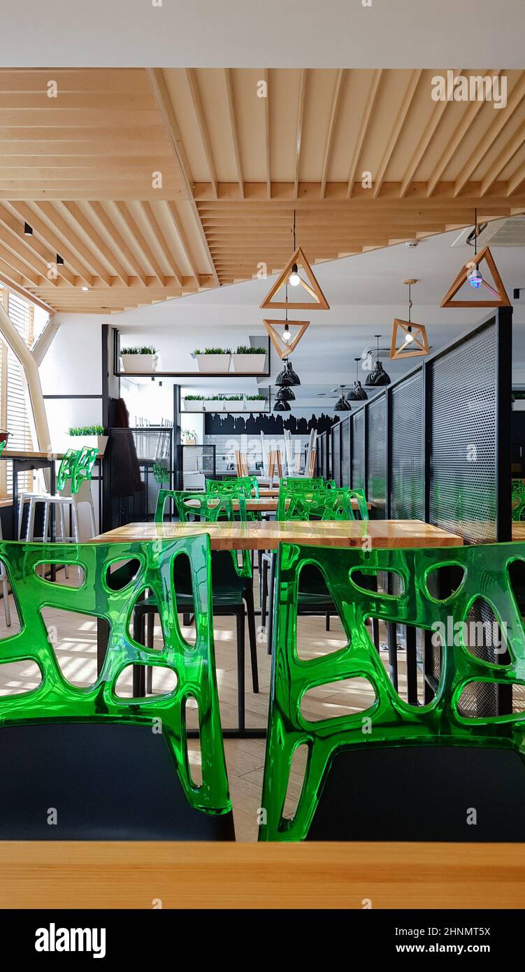 Caffetteria, sala da pranzo senza persone con tavoli in legno e sedie verdi. Interni con elementi in legno e metallo. Moderne aree da pranzo con finestre illuminate. Ucraina, Kiev - 19 febbraio 2021 Foto Stock
