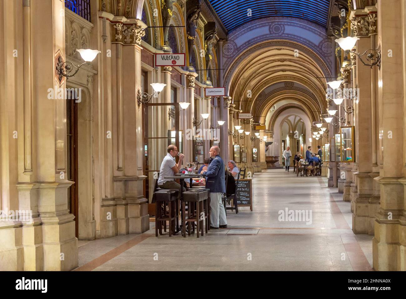 La gente di notte si siede in un ristorante lungo i portici illuminati (portici) nella splendida architettura e maestosa capitale dell'Austria Foto Stock