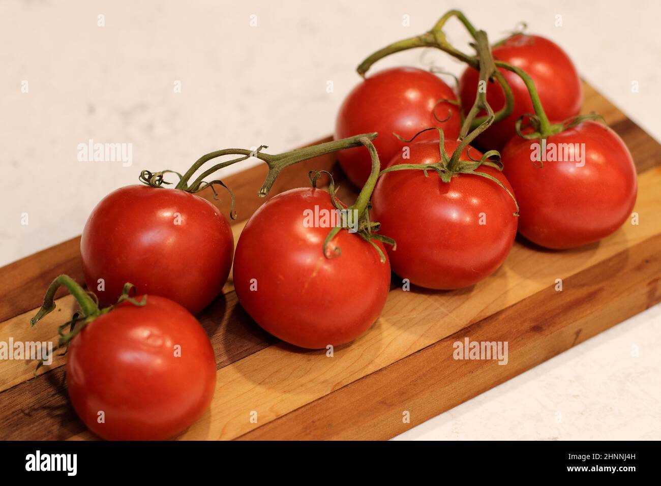Su un banco da cucina ci sono 7 pomodori rossi maturati a vite con steli verdi su un tagliere di legno scuro e chiaro. Pomodori rossi con pomodori verdi Foto Stock