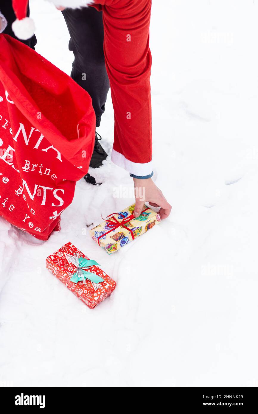 Un uomo vestito come Babbo Natale raccoglie regali in una foresta innevata nella neve, scatole colorate con regali. Foto Stock