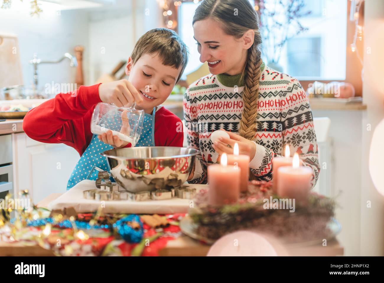 Ragazzo mescolando l'impasto per i biscotti di Natale aiutando la sua madre a cuocere in cucina Foto Stock