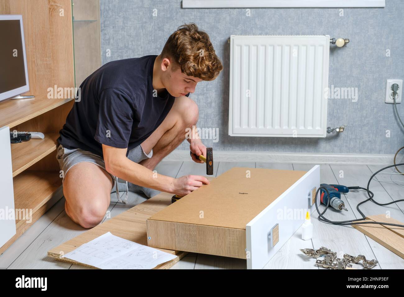 Giovane uomo che lavora con mobili in legno in camera sul pavimento Foto Stock