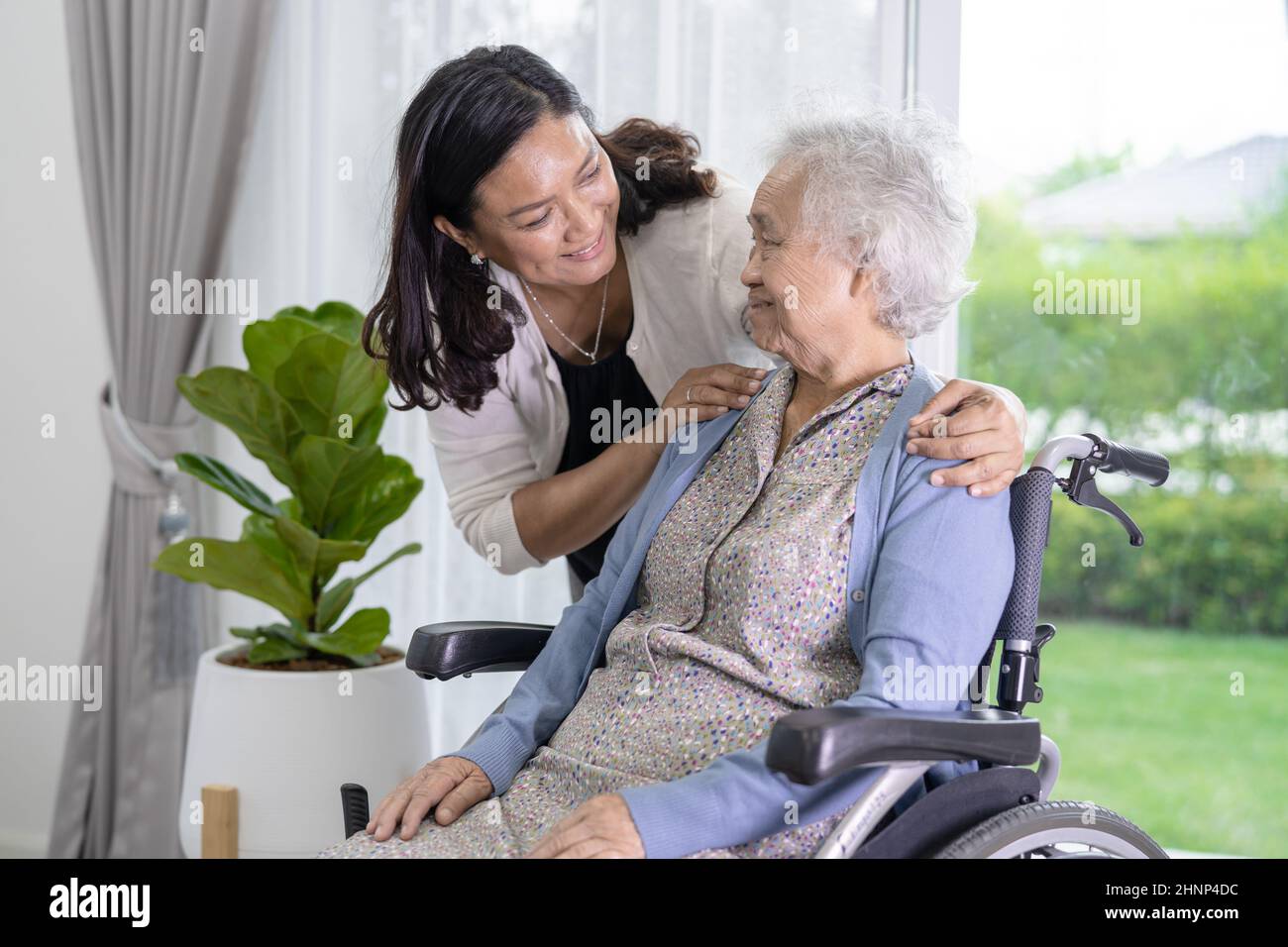 Caregiver figlia aiutare Asian anziano o anziano anziana donna donna seduta su sedia a rotelle e indossare una maschera per proteggere l'infezione di sicurezza Covid-19 Coronavirus. Foto Stock