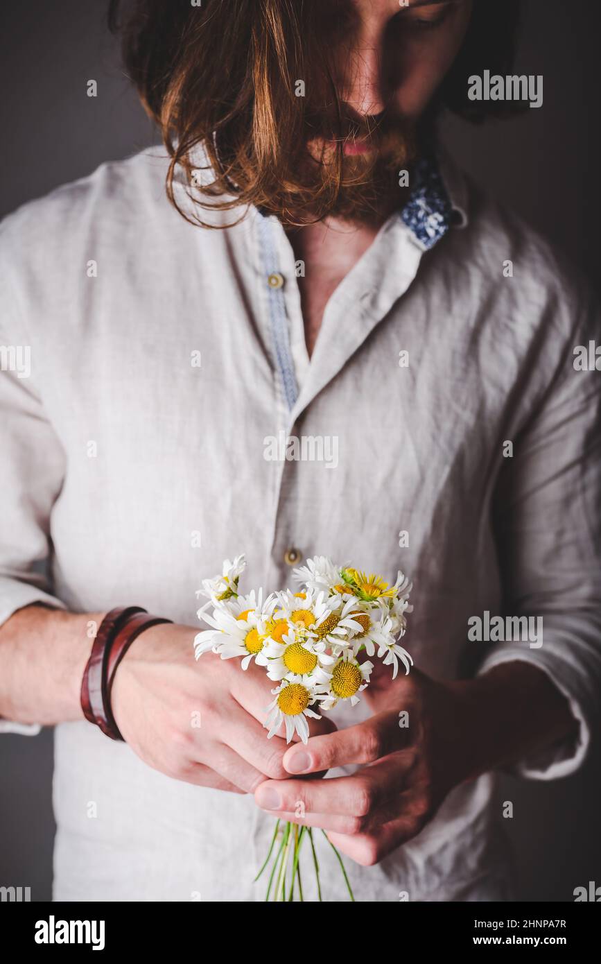 Uomo bearded in camicia di lino con bouquet lungo di tenuta dei capelli Di fiori Daisy in mani Foto Stock