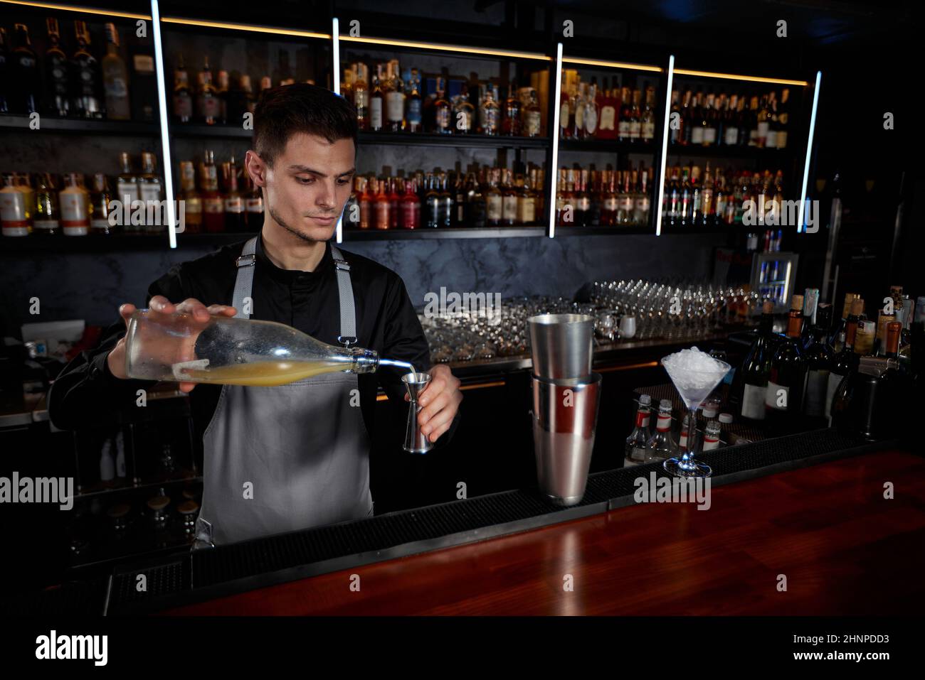 Il barista in grembiule aggiunge l'ingrediente allo shaker Foto Stock