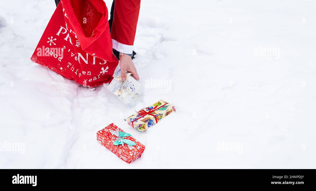 Banner uomo vestito come Babbo Natale raccoglie regali in una foresta innevata nella neve, scatole colorate con regali. Foto Stock