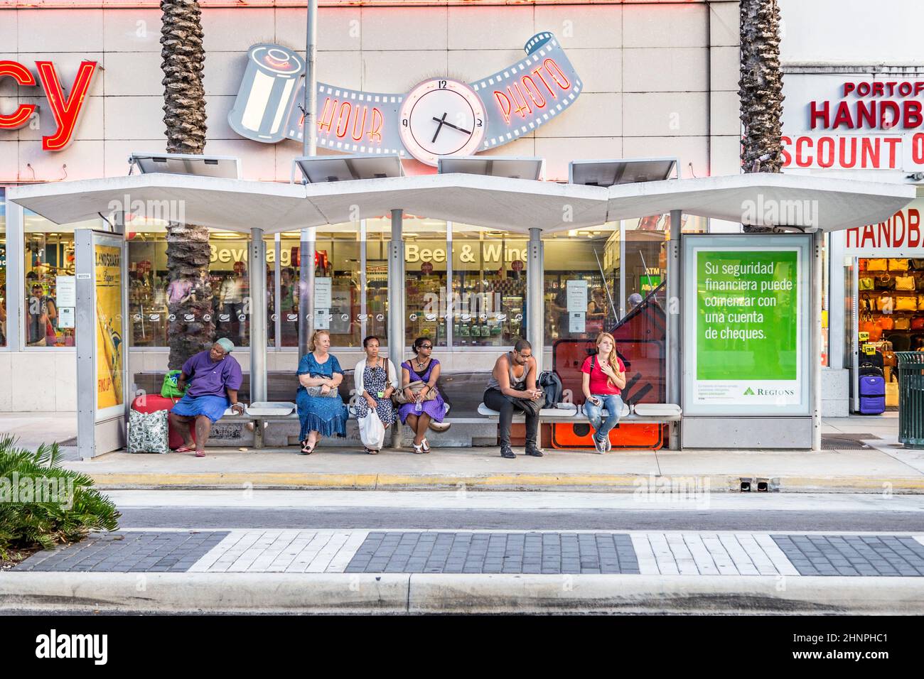 la gente aspetta una fermata dell'autobus di fronte ad un negozio di farmacia. I mezzi di trasporto pubblico a Miami sono coperti da autobus Foto Stock