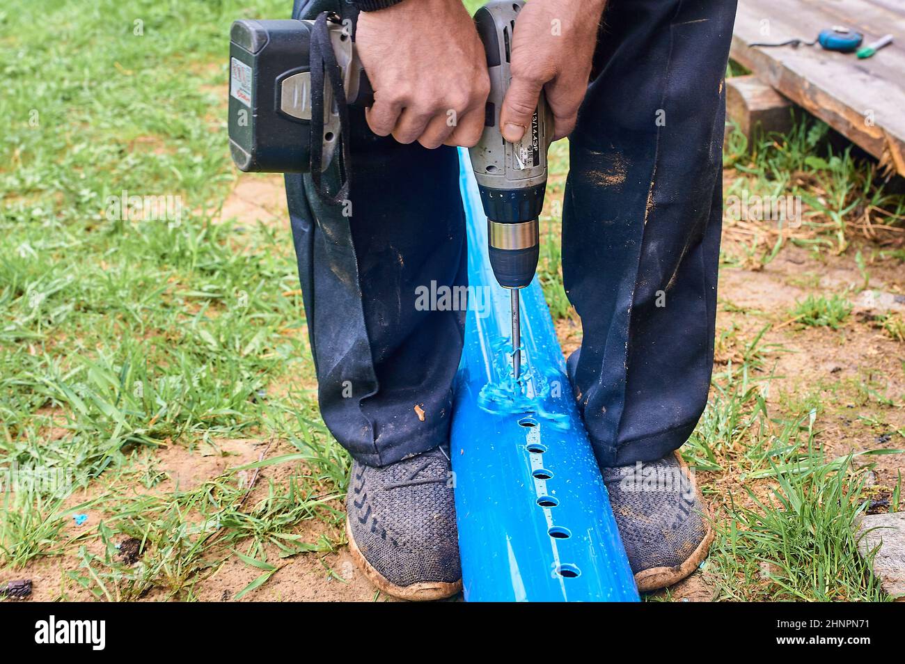 praticare dei fori nel tubo blu di plastica con un cacciavite all'esterno Foto Stock