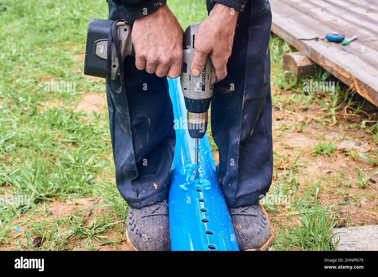 praticare dei fori nel tubo blu di plastica con un cacciavite all'esterno Foto Stock