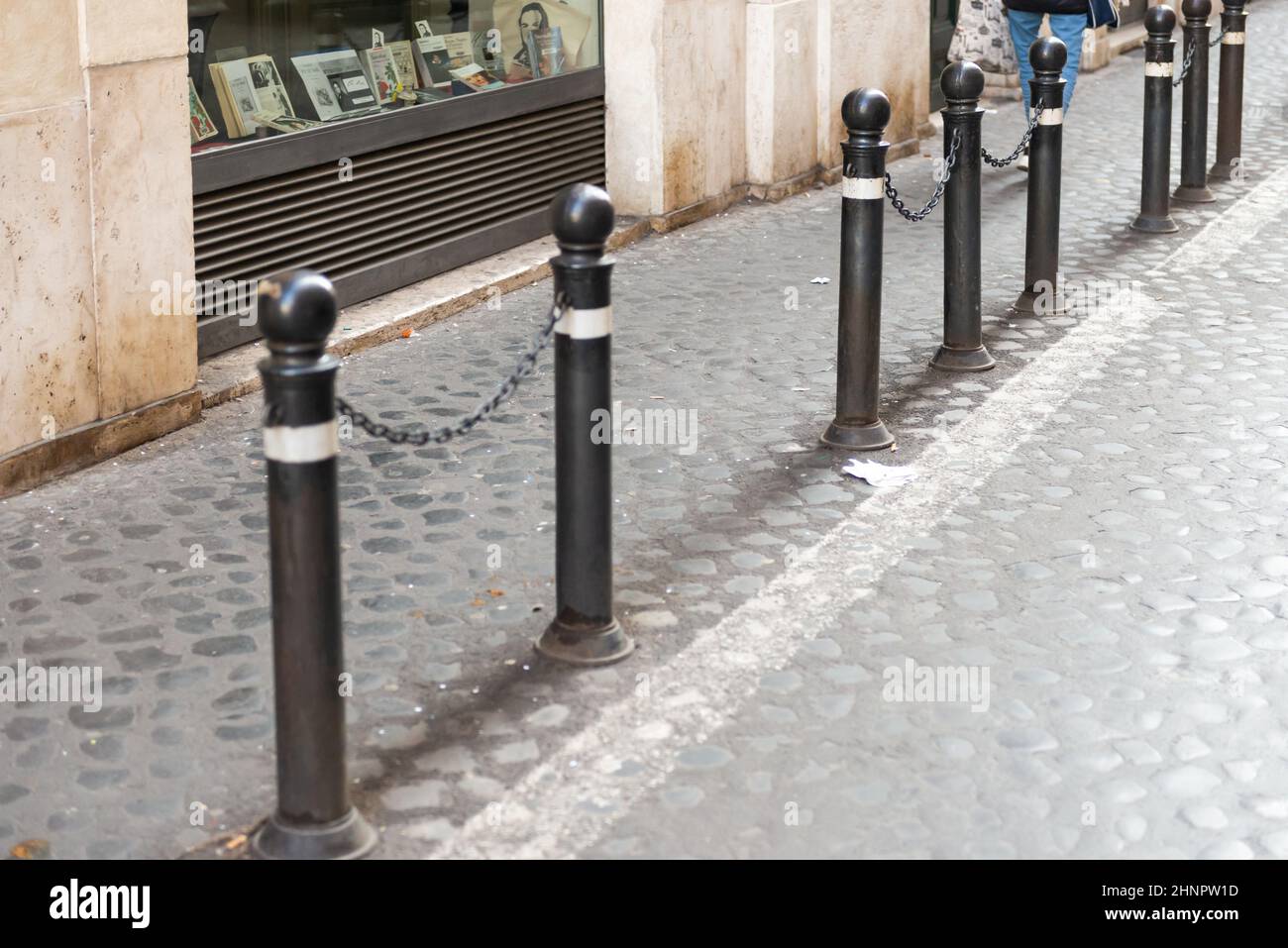 Montanti anti-parcheggio con catene. I pali di metallo separano il marciapiede e la carreggiata sul marciapiede di ciottoli. Foto Stock