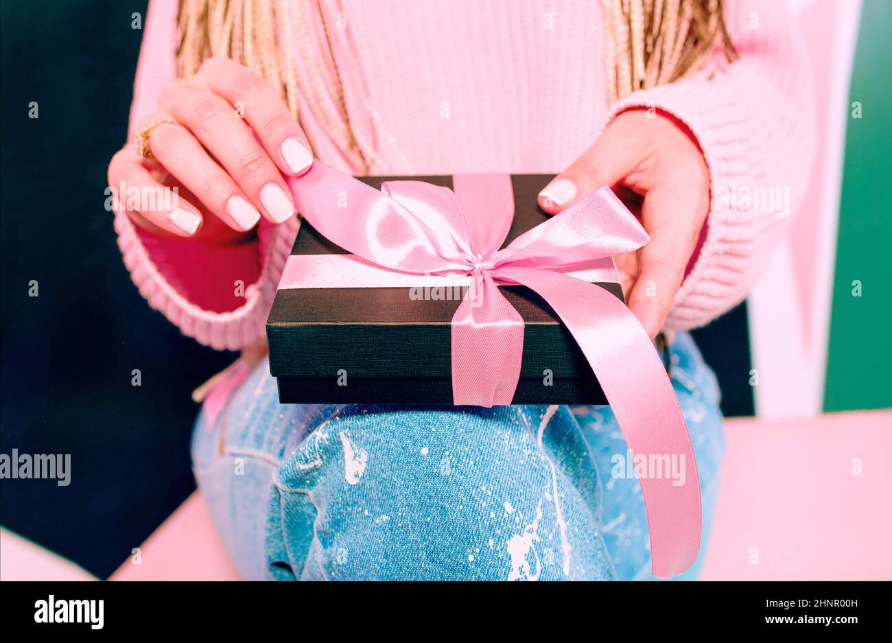 Le mani della donna con manicure rosa che tiene la scatola presente nera con il nastro rosa Foto Stock