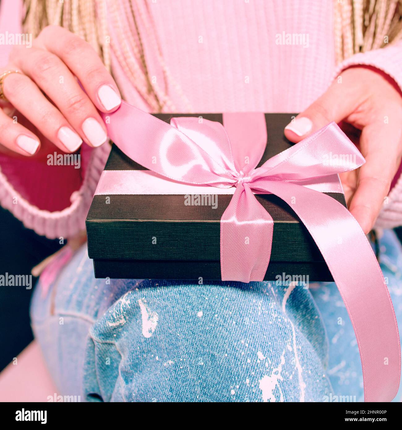 Le mani della donna con manicure rosa che tiene la scatola presente nera con il nastro rosa Foto Stock