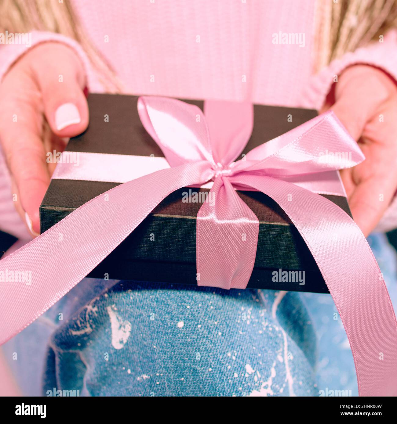 Le mani della donna con manicure rosa che tiene la scatola presente nera con il nastro rosa Foto Stock