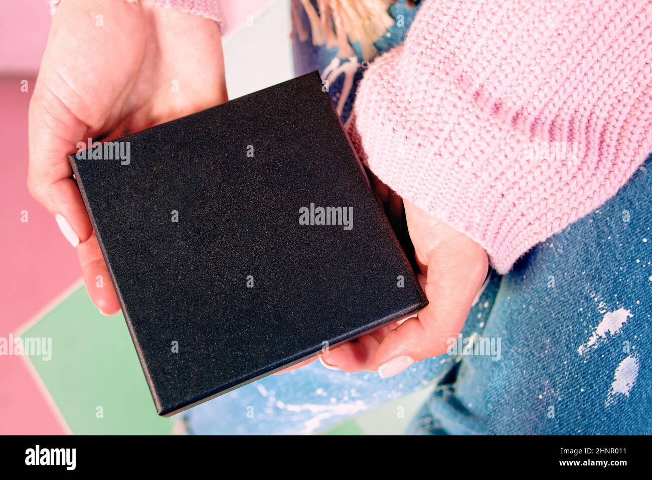 Le mani della donna con manicure rosa che tiene la scatola presente nera Foto Stock