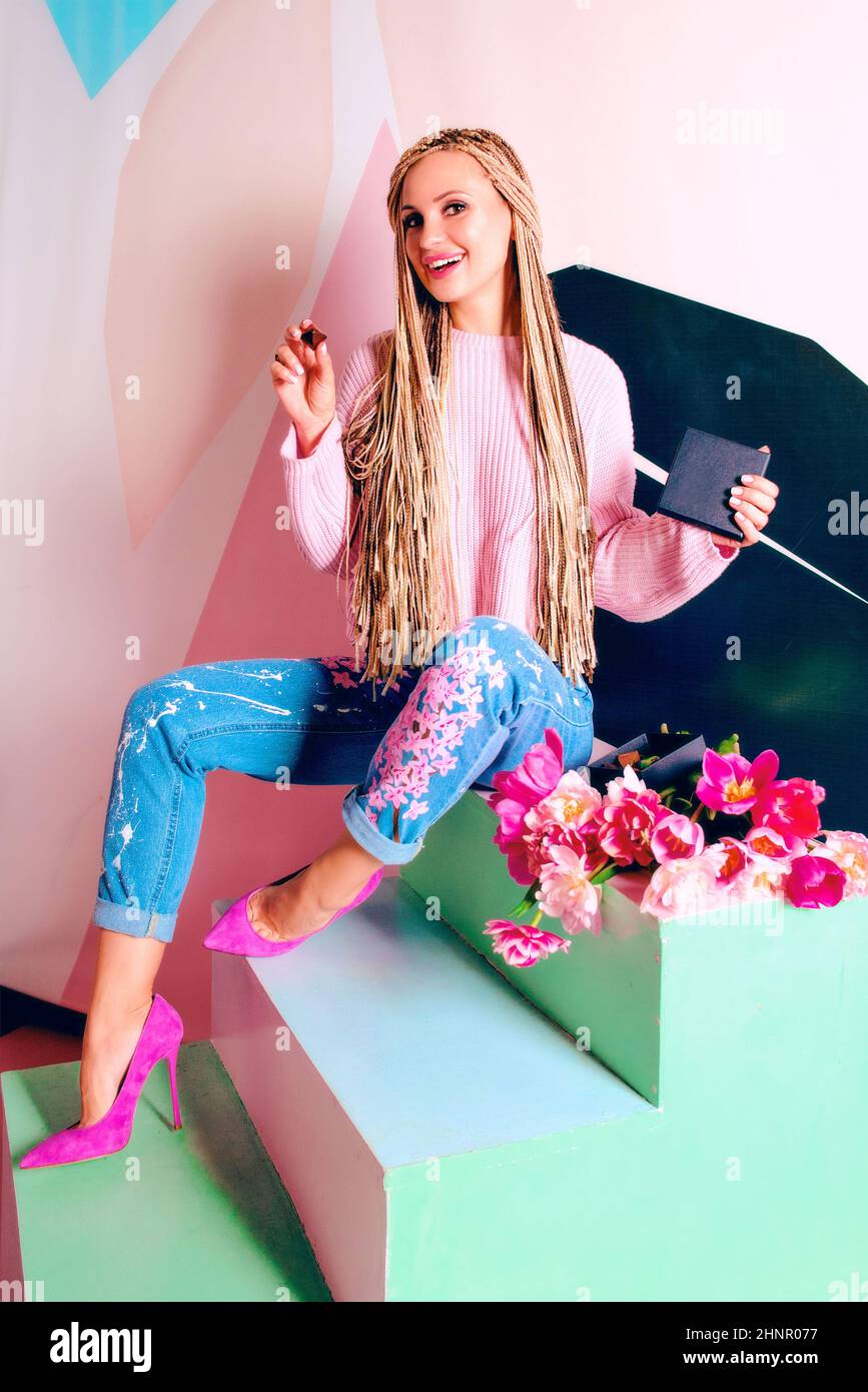 Bella donna bionda con trecce africane rosa che reggono scatola regalo nera Foto Stock