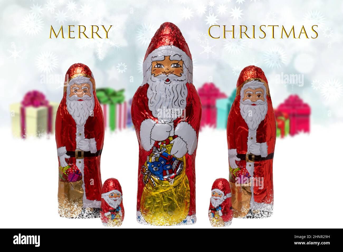 Biglietto di auguri di Natale. Primo piano di vari allegri Babbo Natale di cioccolato avvolto su festive astratte offuscate scatole regalo. Iscrizione Buon Natale. Macro. Foto Stock
