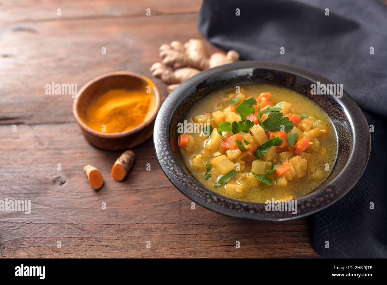 Zuppa di curry con verdure, curcuma e zenzero in una ciotola scura su un rustico tavolo di legno con spazio copia, fuoco selezionato, profondità di campo stretta Foto Stock