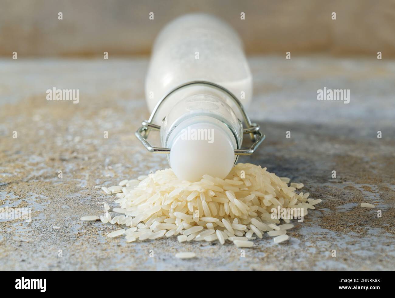 Latte vegano, vista frontale di una bottiglia chiusa giacente su un mucchio di grani di riso su un fondo di pietra grezza, prodotto lattiero-caseario alternativo, primo piano, spazio di copia, Foto Stock